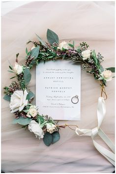 a wedding card with flowers and greenery on top of a bed covered in white sheets