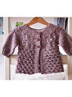 a purple crocheted sweater hanging on a wooden hanger in front of a white chair