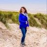 a woman standing on a dirt road in front of grass and sand dunes with her arms around her neck