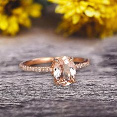 an engagement ring with a peach colored stone and diamonds on the side, sitting on a wooden surface