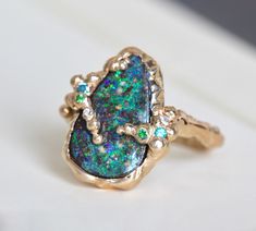 "Our one-of-a-kind 14k yellow gold boulder-opal ring celebrates the natural beauty of this incredible gemstone with a gracefully undulating branch band and hand-hammered texture that emphasizes it's slightly rustic nature: organic minimalism with a brutalist vibe. It's designed to stand on its own as a unique statement, but it also plays well with other pieces adding texture to your daily ring stack. The companion stones, diamond, blue topaz and tsavorite garnet, play to the galactic color of th Organic Minimalism, Boulder Opal Ring, Mode Kimono, Branch Ring, Tsavorite Garnet, Organic Style, Raw Beauty, Hammered Gold, Opal Ring