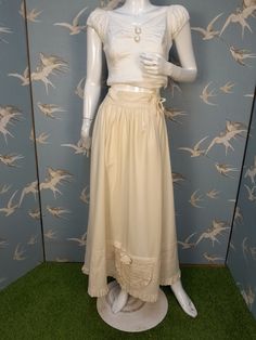 A beautiful cream cotton full length waist petticoat, which I believe dates from the Edwardian era. Made from a nice quality cotton fabric, it`s gathered into a deep waistband which fastens with 2 ties. It has a narrow ruffle at the hem, and an unusual detail of a large pocket just above the hem, which is trimmed with a rosette. In an unusually large size, would fit a current UK 16- 18. Measures 33.5- 35" waist. Length 39". In excellent original condition. There is a small black mark which is vi Vintage Bottoms For Summer Wedding, Beige Cotton Skirt With Lace Trim, Vintage Long Skirt Petticoat, Fitted Vintage Cream Petticoat, Cotton Long Skirt For Wedding, Vintage Cotton Petticoat For Daywear, Cotton Skirt For Summer Wedding, Summer Wedding Cotton Skirt, Vintage Cotton Petticoat With Gathered Skirt