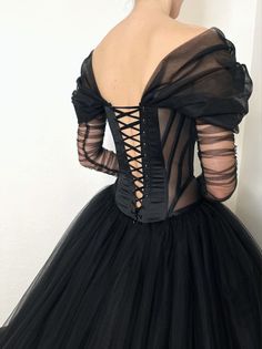 the back of a woman wearing a black dress with sheer sleeves and laces on it