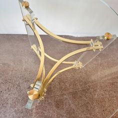 a glass table with metal legs and gold accents on the top, sitting on a marble floor