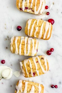 three cranberry rolls with icing on a white counter top next to some fresh cranberries