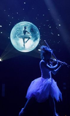 a woman in a tutu playing the violin on stage with an image of a ballerina