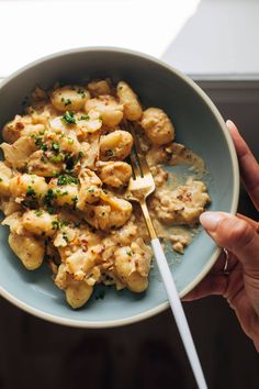 a person holding a fork in a bowl filled with pasta and meat, topped with parsley