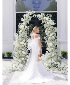 a woman standing in front of a white flower arch