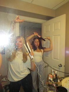 two women standing in front of a mirror holding hairdryer and blow dryer