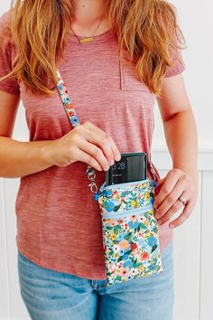 a woman holding a cell phone in her hand and wearing a flowered pouch with an adjustable strap