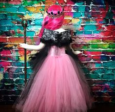 a mannequin dressed in a pink and black dress standing next to a brick wall