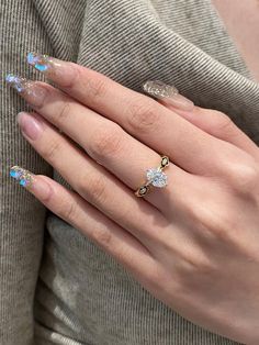 a woman's hand with clear manies and gold rings on her fingers, wearing a grey sweater