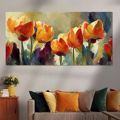 an abstract painting of orange flowers on a white wall above a gray couch with yellow and red pillows