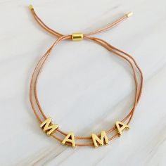 This beautiful MAMA bracelet is made of a slim satin thread with a simple golden font. Its clean, minimalist design features adjustable drawstring size for easy fitting, with each letter that moves independently around the thread. Perfect for any mom.Dimensions: approximately up to 10 inches perimeter fully adjustable with a slide18k gold plated brassLead and Nickel freeEthically sourcedMade in ChinaShips from USA Adjustable Length Gold Jewelry With Nylon Cord, Gold Jewelry With Adjustable Nylon Cord, Casual Gold Bracelet With Adjustable Cord, Everyday Nylon Cord Jewelry, Adjustable Bracelets With Nylon Cord, Adjustable Custom Name Friendship Bracelets For Everyday, Adjustable Gold Casual Friendship Bracelets, Gold Adjustable Casual Friendship Bracelets, Adjustable Name Bracelet As Gift For Mom