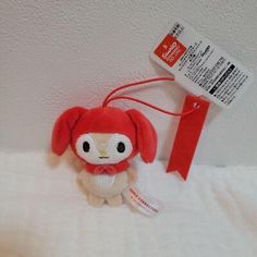 a small red stuffed animal sitting on top of a white bed next to a tag