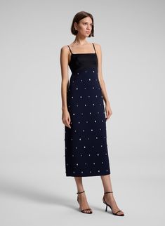 The Alana Dress combines deep rich navy cady fabric and black high-shine satin, adorned with scattered, teardrop-shaped crystals, offering a unique take on festive embellishment. This midi silhouette features a straight skirt, a bustier-inspired bodice with adjustable straps, and delicate side cutouts with an open back for a modern, striking look. Shop Dresses. Styling Tip: Pair with metallic heels and a sleek clutch for an elegant dinner or holiday soirée. Embellished Silk Midi Dress For Formal Occasions, Chic Embellished Silk Midi Dress, Formal Embellished Silk Midi Dress, Evening Midi Dress With Contrast Sequin, Blue Embellished Evening Midi Dress, Blue Embellished Midi Dress For Evening, Holiday Soiree, Evening Midi Dress, Shaped Crystals