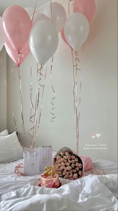 pink and white balloons are on the wall above a bed with a cake, gift bag and flowers