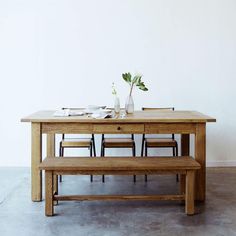 a wooden table with four chairs and a bench in front of it, against a white wall