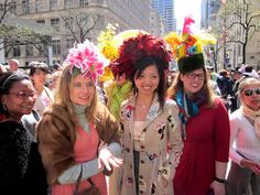 three women standing next to each other in front of a crowd wearing fancy hats and scarves