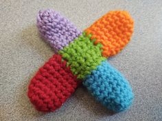 four crocheted slippers are laying on the floor, one is multicolored