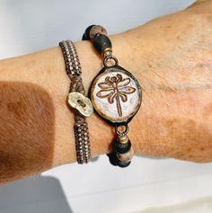 Unique Glass Dragonfly connector sits with African Recycled Glass beads in black and mottled brown. This bracelet is sized for the small wrist at 7 inches in length. Read below to determine you sizing. To ensure the desired fit of bracelets: Measure your wrist and add 1/2 to 3/4 inch. Think about where you want the particular bracelet to hang - snug, a bit loose or looser to wear lower on your hand.  Example: my wrist measures 6.75" in length  A 7" length  is tight but wearable A 7.25" length is the size I prefer  A 7.50" length is doable, a bit looser but still wearable  To see all my unique handmade jewelry visit www.majidesigns.etsy.com Shipping is FREE in the USA! My turnaround time is 1-2 days. I ship 1st class mail.  Any additional questions:  Majidesignsjewelry@gmail.com Fall Earth Tones, Glass Dragonfly, Dragonfly Bracelet, Recycled Glass Bead, Ready For Fall, Unique Handmade Jewelry, Recycled Glass, Bead Bracelet, Earth Tones