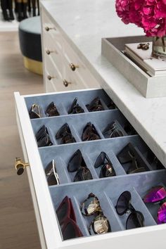 an open drawer with many pairs of sunglasses in it and a vase filled with flowers