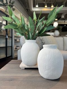 two white vases sitting on top of a wooden table in front of a couch