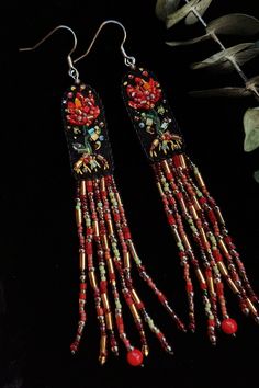 red and gold beaded earrings with long tassels on black surface next to plant