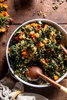 a bowl filled with rice and spinach on top of a wooden table next to flowers