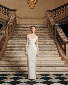 a woman in a wedding dress standing on the stairs with her hands behind her back