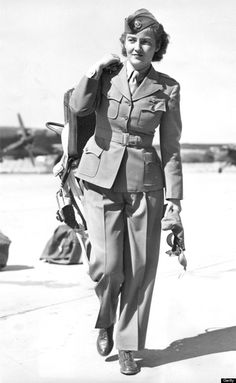 an old black and white photo of a woman in uniform walking on the tarmac