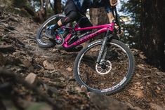 a person riding a pink bike on a rocky trail in the woods with trees and rocks