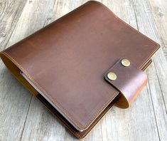 a brown leather notebook on a wooden surface with two buttons in the front and one at the back