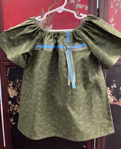 This adorable little peasant-style dress is made of a cotton/poly blend fabric in olive green with blue and green dragonfly print. The ribbons (excellent quality double side satin) are slightly off-set at the neckline and are olive green & blue. There's a beautiful little dragonfly button accenting the ribbons. It is machine washable (I recommend cold water, gentle cycle) - tumble dry.  Ironing will likely be required after laundering. This is a toddler size 3 and is 18.5" from the neckline to the hem.  My husband is Passamaquoddy, I am Mexican-American. I have been making custom ribbon shirts and regalia for members of the local tribes in Maine for a 12+ years. Green Cotton Peasant Dress, Peasant Style Dress, Dragonfly Print, Dragonfly Prints, Green With Blue, Green Dragonfly, Ribbon Dress, Custom Ribbon, Ribbon Shirt