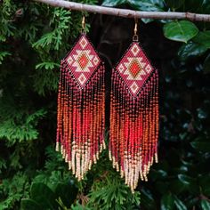 two pairs of red and white beaded earrings hanging from a branch with green leaves in the background