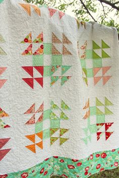 a quilt hanging on a clothes line with trees in the background and grass behind it