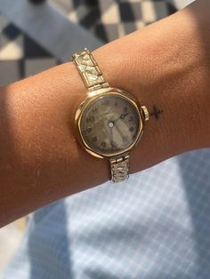 a close up of a person's wrist with a watch on her arm and a checkered shirt in the background