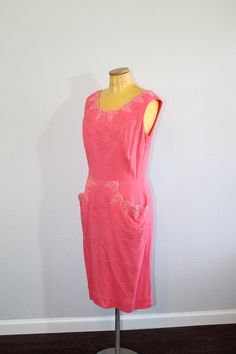 "The most perfect and prettiest 1950s pink wiggle dress! It features beautiful lace at the neck, two huge pockets in front, studs in floral patterns, and rhinestones. FEATURES: * Label: None * Circa: 1950s * Materials: Unmarked. Feels like a woven cotton, possibly with some rayon * Color: Pink (almost a salmon, but more pink) * Pattern: Floral stud pattern * Length: Below knee * Waist: Fitted natural waist * Sleeves: Sleeveless * Neckline: Scoop * Closure: Metal zipper up the back with hook and Pink Fitted Vintage Dress, Pink Fitted Dress With Pockets, Pink Fitted Dresses With Pockets, Fitted Pink Dresses With Pockets, Pink Sleeveless Dress For Vintage Fashion, Pink Elegant Vintage Dress, Elegant Pink Vintage Dress, Pink Fitted Vintage Dress With Lining, Fitted Vintage Pink Dress Lined