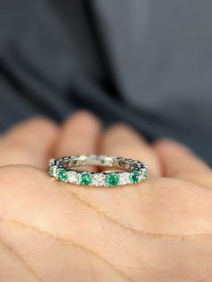 a person holding an emerald and diamond ring in their hand