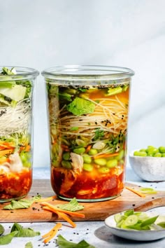 two glass jars filled with food sitting on top of a wooden cutting board next to bowls and spoons