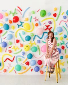 a woman is sitting on a stool in front of a wall with balloons and shapes