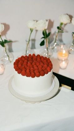 a white cake with red icing on a table next to candles and flowers in vases