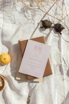 a table topped with an open book next to two lemons and sunglasses on top of a white blanket