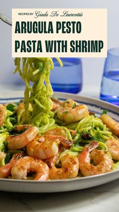 A white and blue plate with spaghetti and shrimp plated on it. The pasta has a light green sauce and pieces of chopped arugula on it and the shrimp are nicely grilled with spices sprinkled on top. There are two blue glasses in the background for styling purposes. Pesto Pasta With Shrimp, Pasta With Shrimp, Arugula Pesto, Pasta Noodle Recipe, Cooking 101, Western Food, Grilled Shrimp, Seafood Dinner, Pesto Pasta