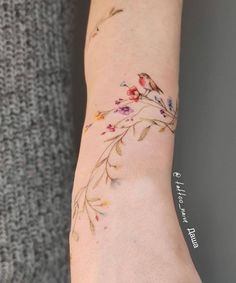 a woman's arm with flowers on it and a bird sitting on the branch