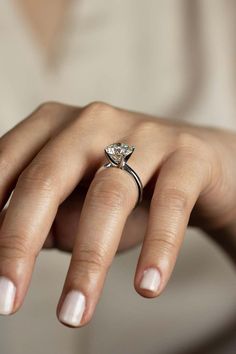 a woman's hand with a diamond ring on her left hand and white nails