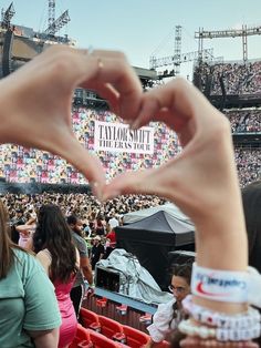 two hands making a heart shape in front of a crowd at a music festival,