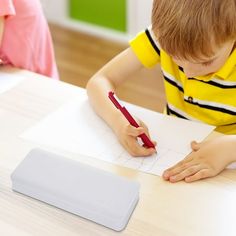 a young boy sitting at a table writing on paper with a red pen in front of him