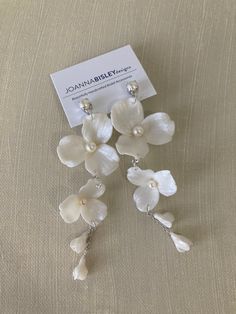 three white orchids with pearls hanging from the end of each earring, on a beige background