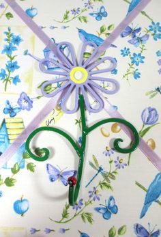 a purple flower is attached to a green hook on a white background with blue flowers and butterflies